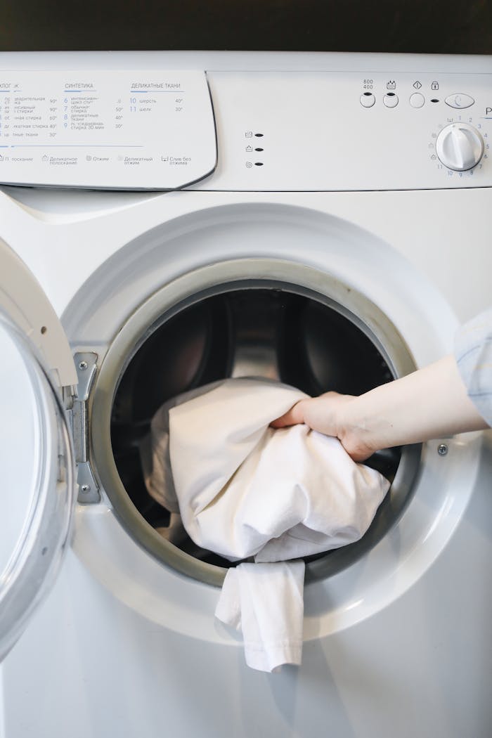 Close-up of a persons hand putting laundry into a front-loading washing machine.